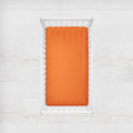 Orange fitted sheet on a white crib with a light gray background. orange crib sheet - the creative raccoon