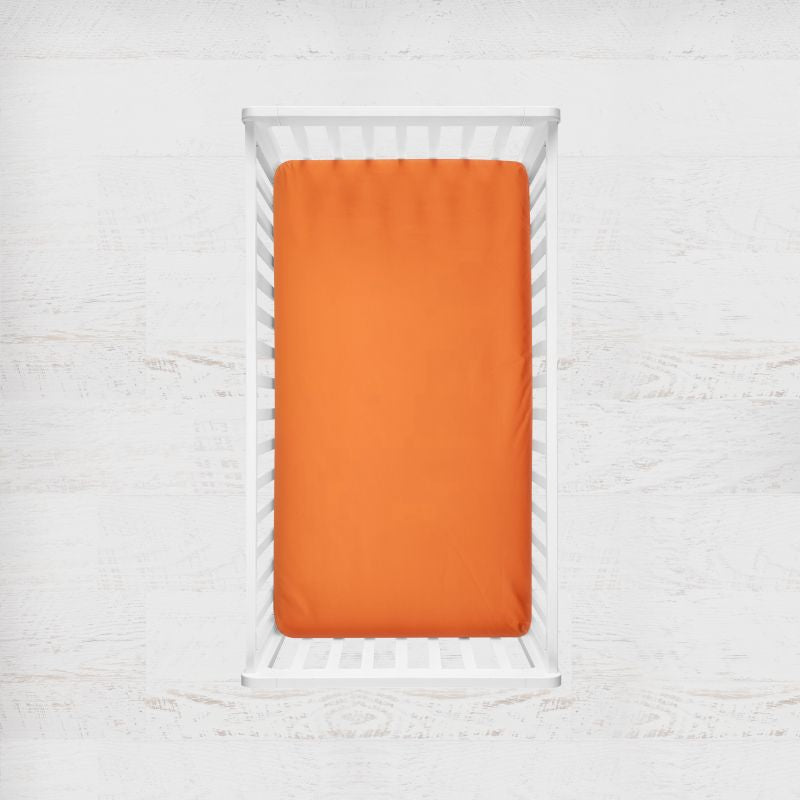 Orange fitted sheet on a white crib with a light gray background. orange crib sheet - the creative raccoon