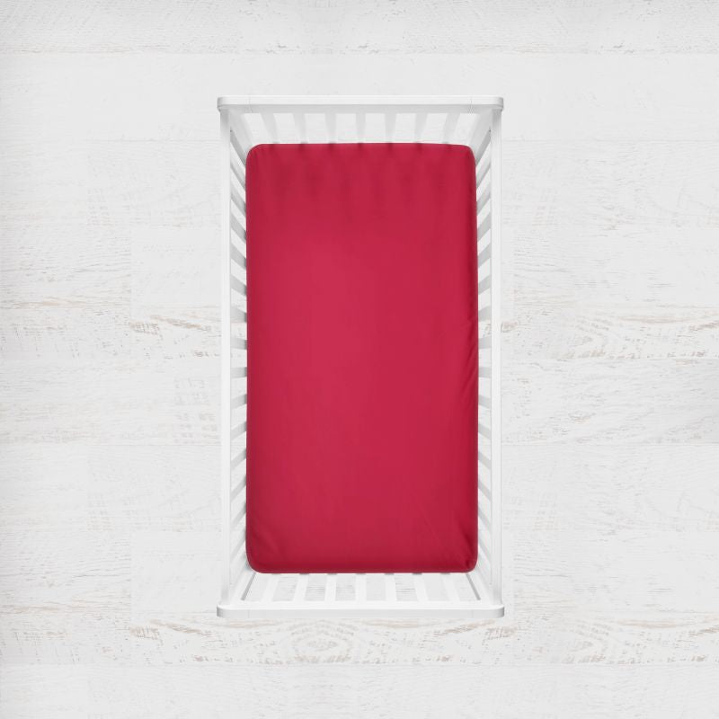 Red fitted sheet on a white bed with a light gray background. rich red crib sheet - the creative raccoon