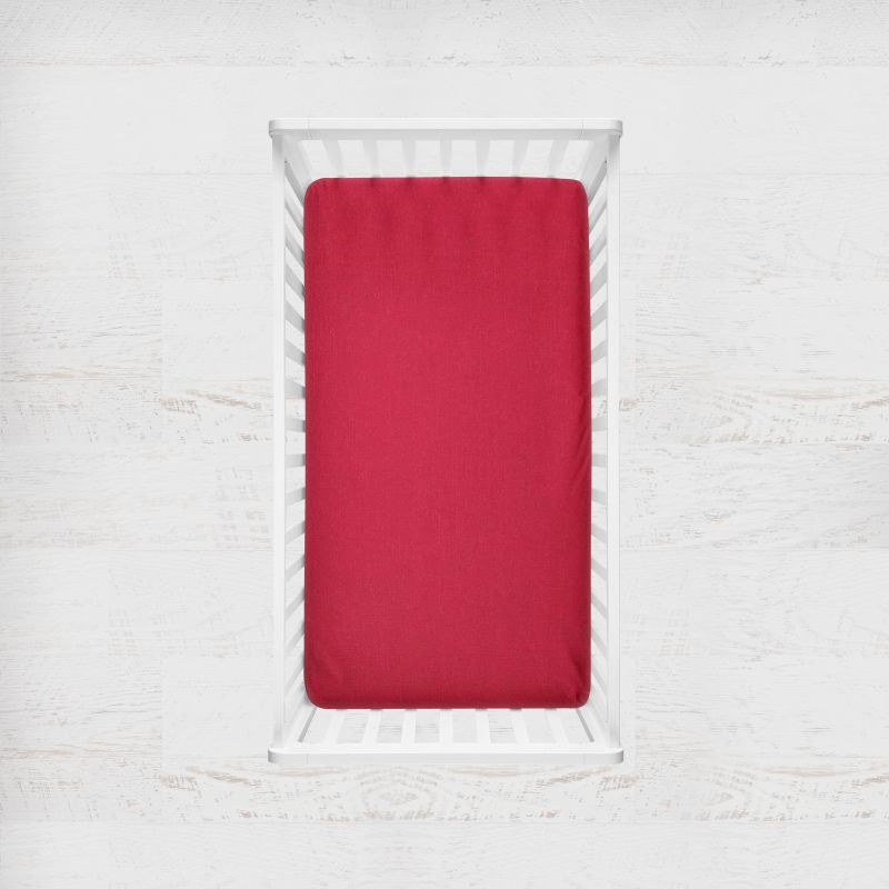 Red fitted sheet on a white bed frame against a white textured wall. scarlet red crib sheet - the creative raccoon