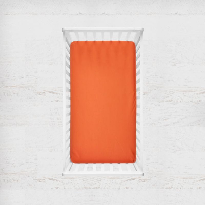 Orange fitted sheet on a white crib with a light gray background. tangerine orange crib sheet - the creative raccoon