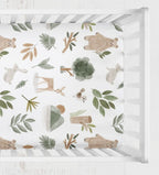 A top-down view of a crib sheet with a woodland pattern of bears, rabbits, deer, leaves, and trees in muted green, brown, and beige tones. woodland animals crib sheet - The Creative Raccoon